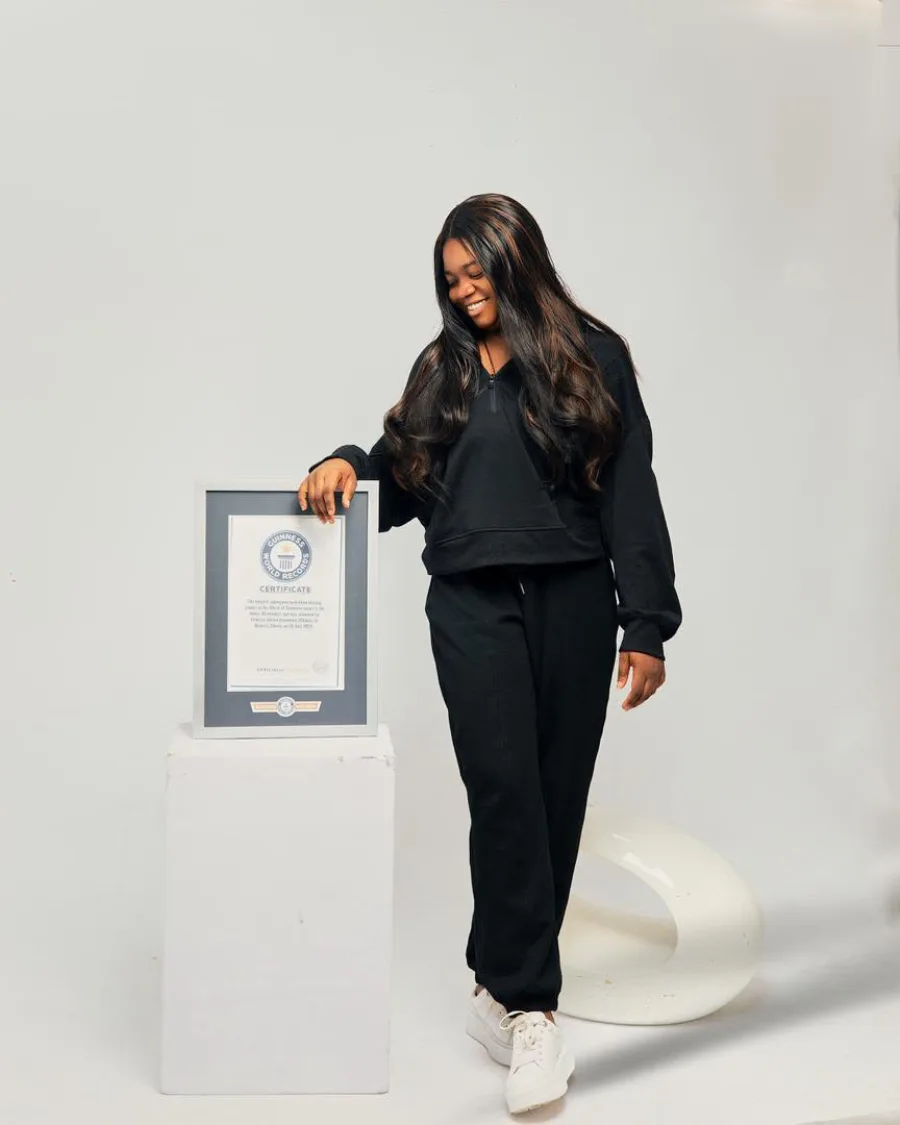 Vanessa Selase Azoumaro standing beside her framed Guinness World Records certificate on a white plinth.